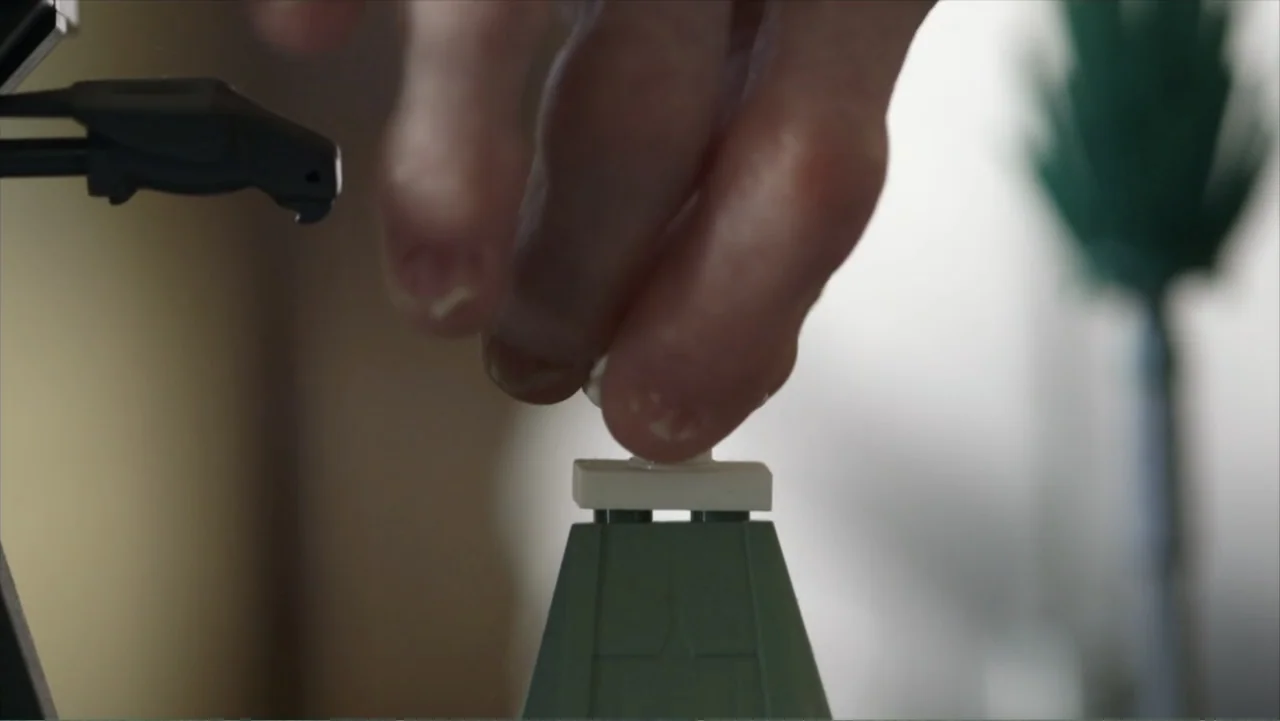 Life According to Sam (2013) movie still: closeup — A close-up view shows a hand interacting with small plastic construction toy components. The…