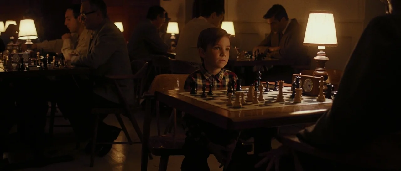 Pawn Sacrifice (2014) movie still: medium — A dimly lit club filled with several people sitting at tables playing chess games. A young girl sits at…