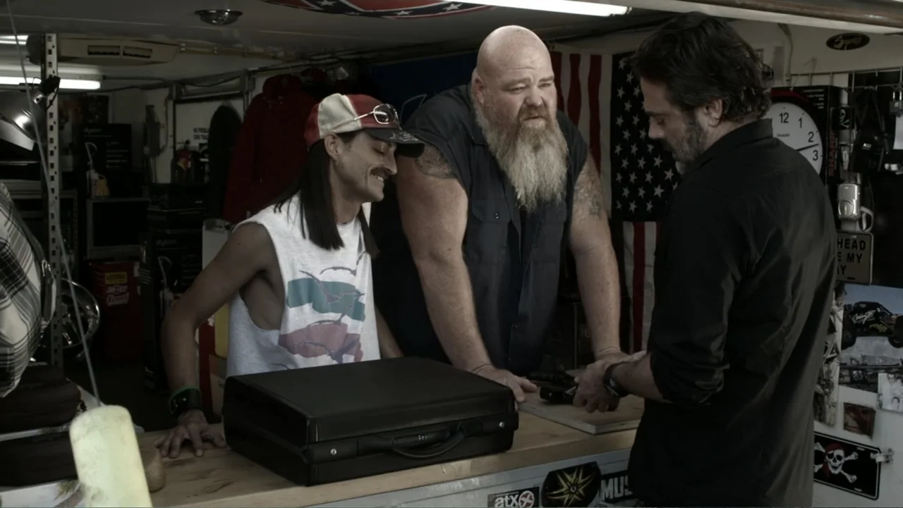 The Messenger (2015) movie still: medium — A cluttered garage interior features tools and an American flag hanging on the wall. Three men gather…