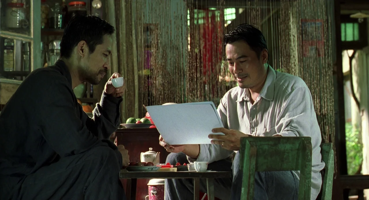 The Vertical Ray of the Sun (2000) movie still: medium — A modest room contains a small wooden table with tea cups and fruit plates. Two men sit…