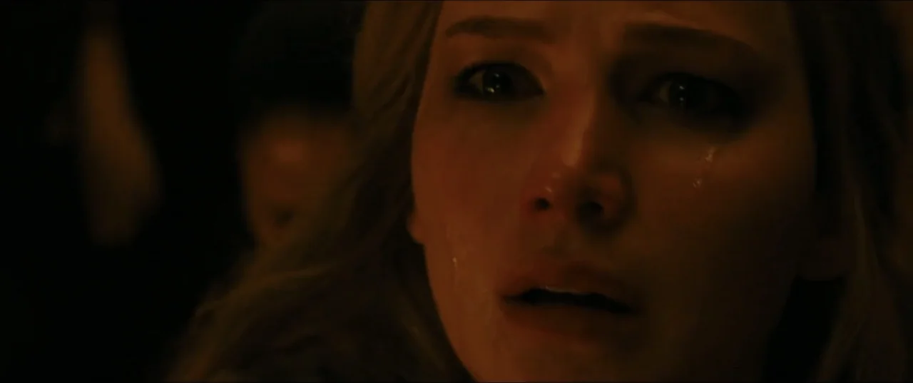 mother! (2017) movie still: closeup — A dimly lit interior space with shadows hiding all environmental features. A young woman looks toward the…