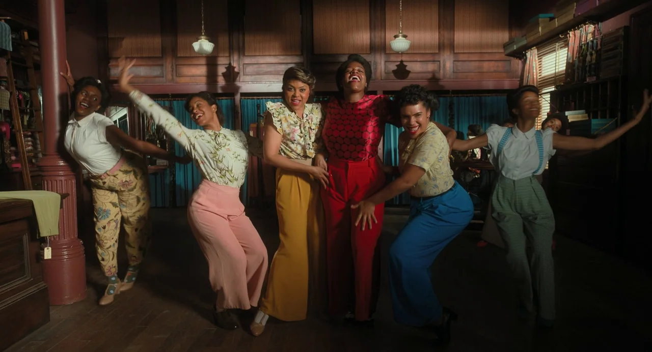 The Color Purple (2023) movie still: fullbody — A 1940s retail space features dark wood paneling, hanging light fixtures, and fabric storage. Five…