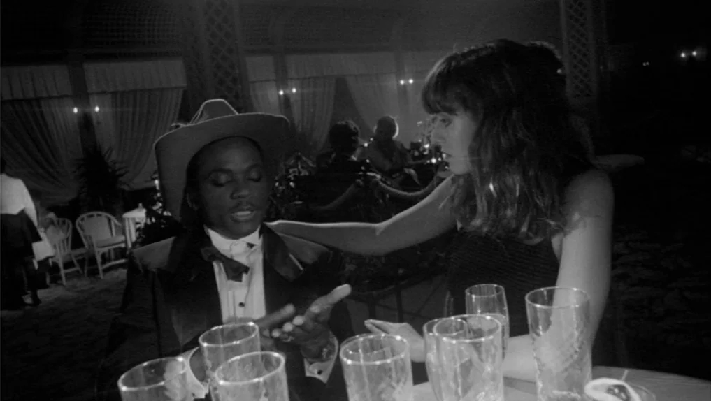 Under The Cherry Moon (1986) movie still: medium — A dimly lit lounge featuring tables surrounded by chairs and curtained wall alcoves. A man in a…