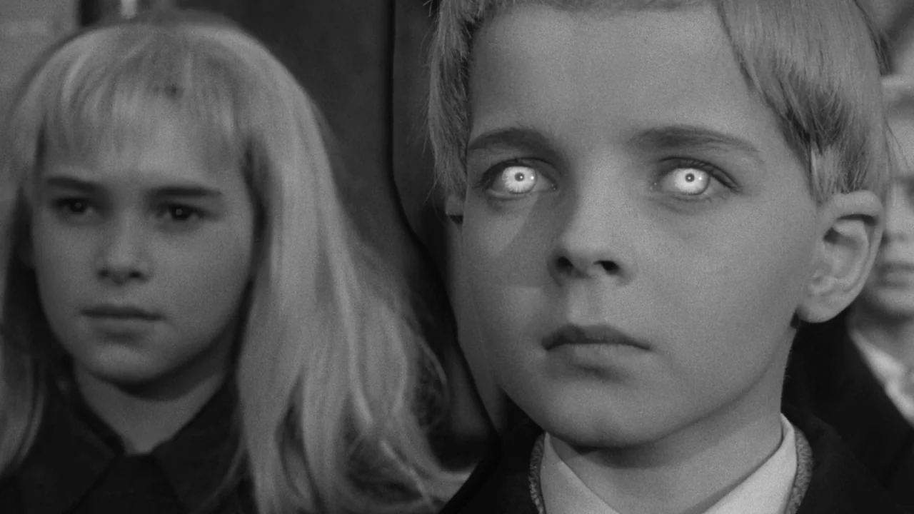 Village of the Damned (1960) movie still: medium — Two children with glowing eyes stare ahead in a bright, institutional space. The boy is in the…