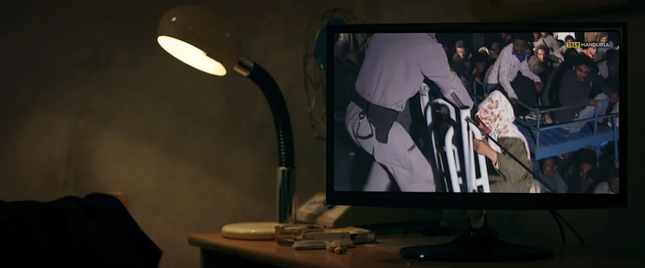 Taranta On the Road (2017) movie still: medium — A dimly lit room contains a desk with a lamp and a computer monitor. The monitor screen shows a…