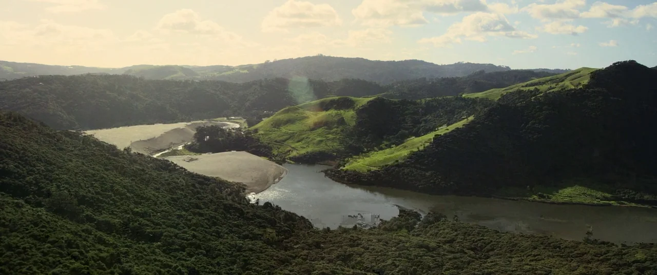 Hunt for the Wilderpeople (2016) movie still: establishing — A wide aerial view shows a valley featuring a winding river and sand dunes. Rolling…