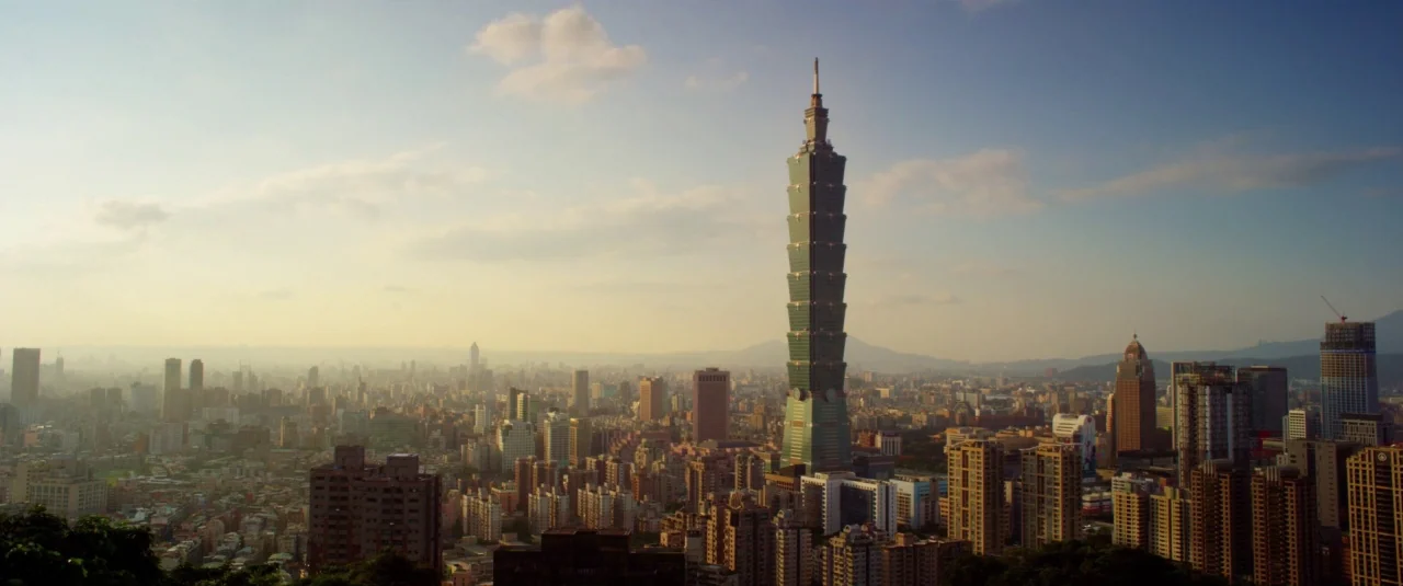 Lucy (2014) movie still: establishing — A panoramic high-angle view shows the dense metropolitan landscape of Taipei under soft sunlight. The…