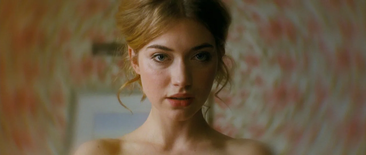 Filth (2013) movie still: closeup — A close portrait of a young woman against a blurred floral patterned wall. She gazes forward with a focused look.