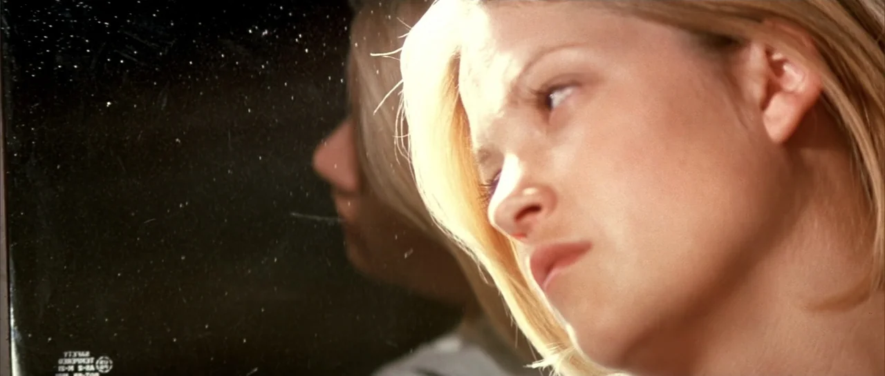 Jeepers Creepers 2 (2003) movie still: closeup — A woman's face is partially reflected on the dirty glass surface of a car window. The sunlight…