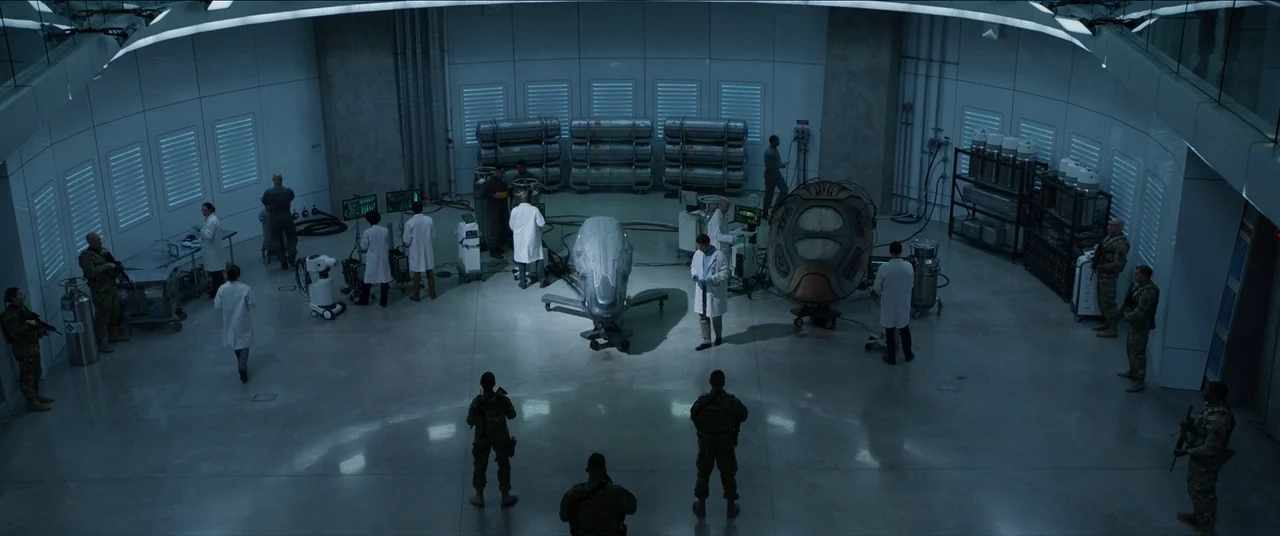 The Predator (2018) movie still: wide — A spacious high-tech laboratory with white curved walls contains scientists and armed soldiers. People…