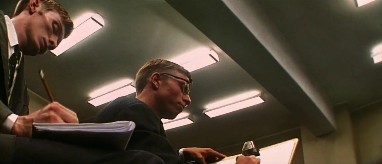 Dancer in the Dark (2000) movie still: medium — A room with rows of overhead fluorescent lights mounted to a concrete ceiling. Two young men in…