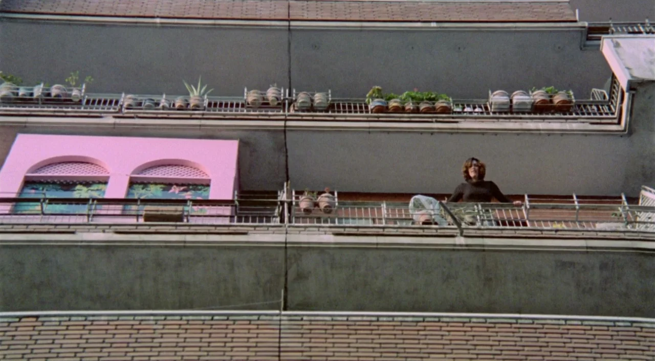 What Have I Done To Deserve This? (1984) movie still: wide — A multi-story residential building features concrete balconies lined with various…