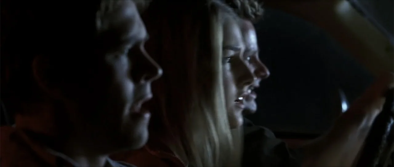 Joy Ride (2001) movie still: medium — Inside a dark vehicle at night, three people sit in the front seat together. The subjects look ahead with open…