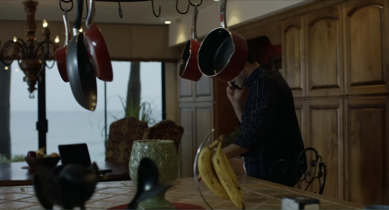 Instantes Capturados (2022) movie still: medium — A residential kitchen features dark wood cabinets and a tile countertop with hanging cookware. A…