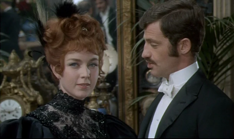 The Thief of Paris (1967) movie still: medium — A dimly lit indoor space with ornate gold-framed mirrors and clocks. A woman with red hair and a man…