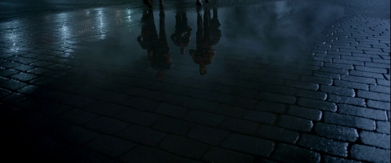 Resident Evil: Retribution (2012) movie still: wide — A dark cobblestone ground is covered with thin water, creating deep reflections of figures.…