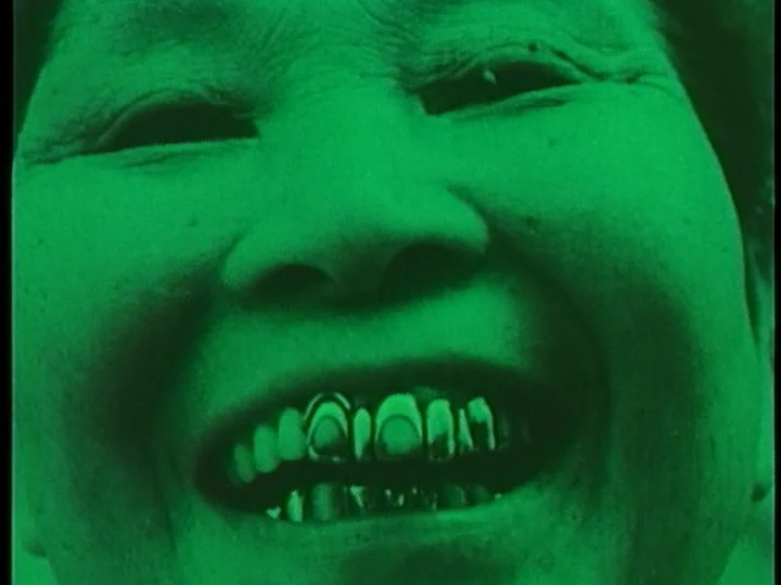The Cage (1964) movie still: closeup — An extreme close-up of a smiling face fills the frame. The entire image is filtered with a vibrant green…