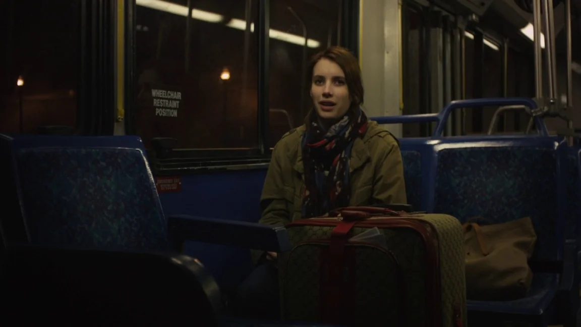 Adult World (2013) movie still: medium — An interior of a public bus at night with blue molded plastic seats. A young woman sits in a seat with a…