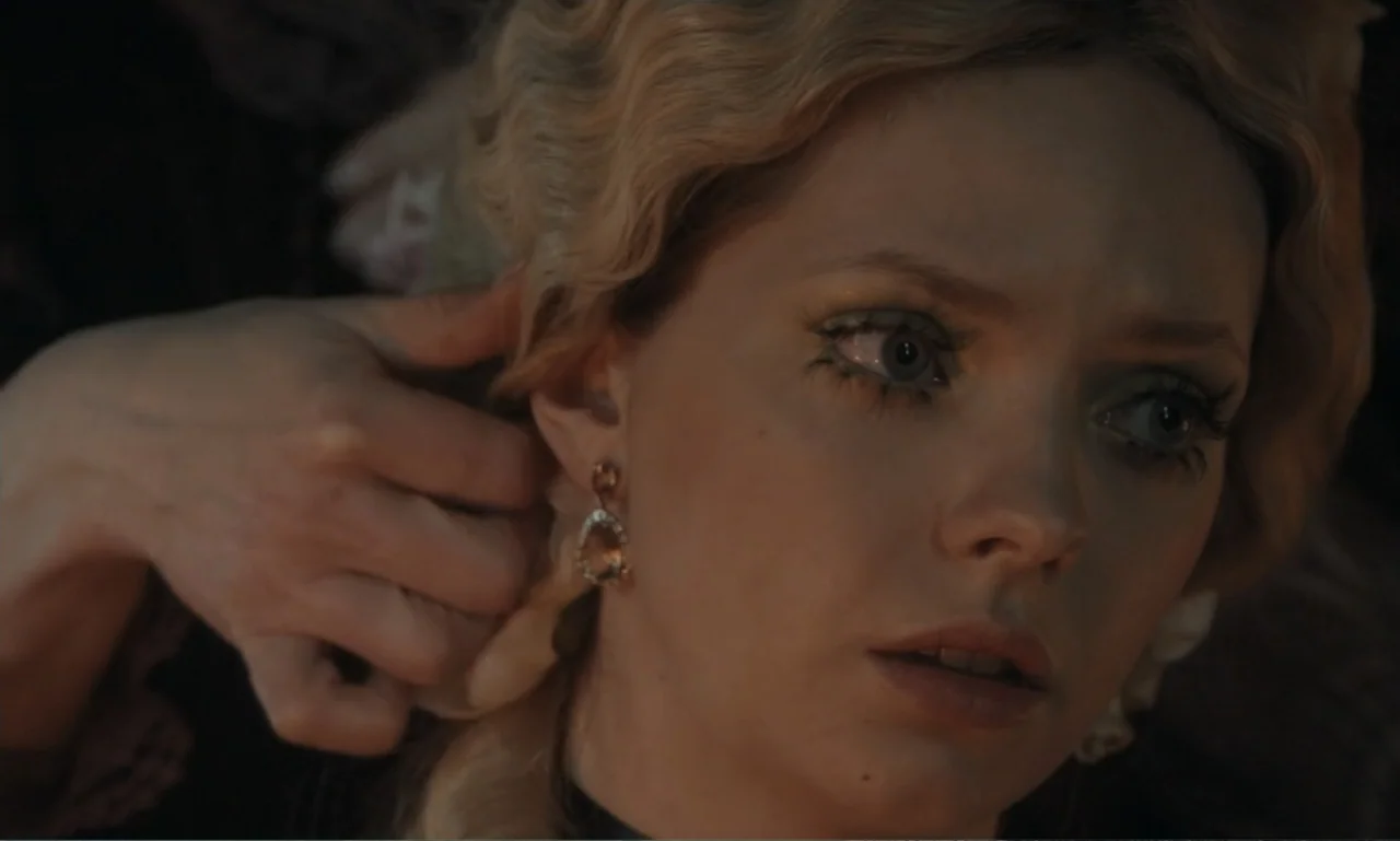The Ugly Stepsister (2025) movie still: closeup — An interior space features a close view of a young woman during a dressing session. Someone…