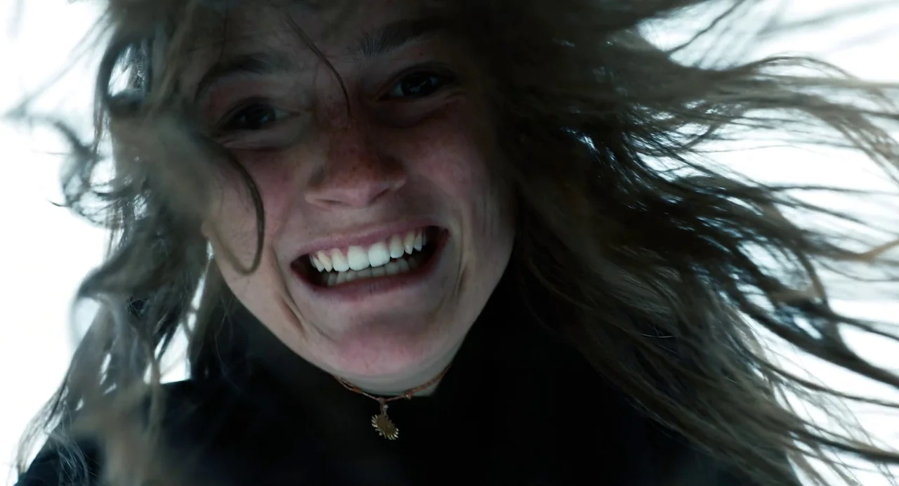 Hellbender (2021) movie still: closeup — An outdoor setting with bright white sky dominates the background behind the subject. A woman leans toward…