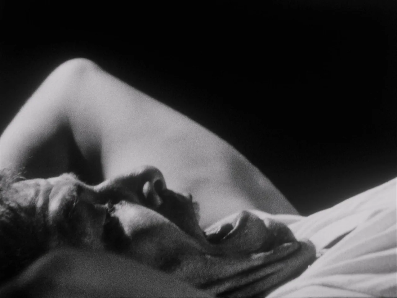 Subconscious Cruelty (2000) movie still: closeup — A man lies on a surface against a dark background in low light. The focus is on the profile of…
