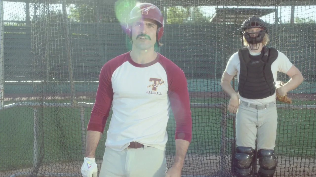 Everybody Wants Some!! (2016) movie still: medium — Two baseball players stand inside a chain-link batting cage on a sunny day. The batter is in the…