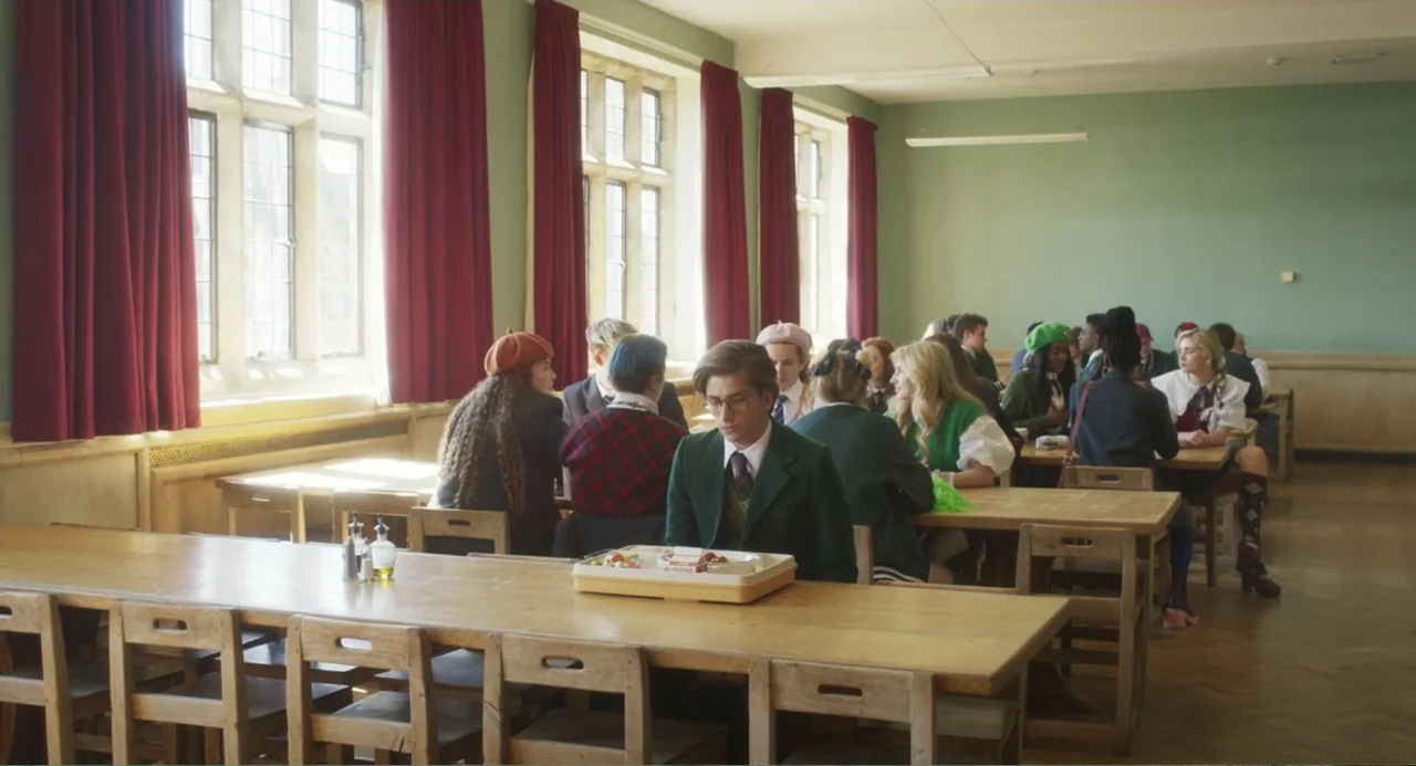 How to Date Billy Walsh (2024) movie still: wide — A long, institutional hall with green walls and tall windows with red curtains. A group of…