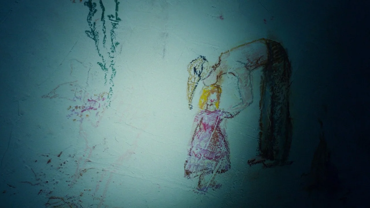 Girl on the Third Floor (2019) movie still: closeup — A textured wall shows a crude crayon drawing of two human figures. A concentrated light beam…