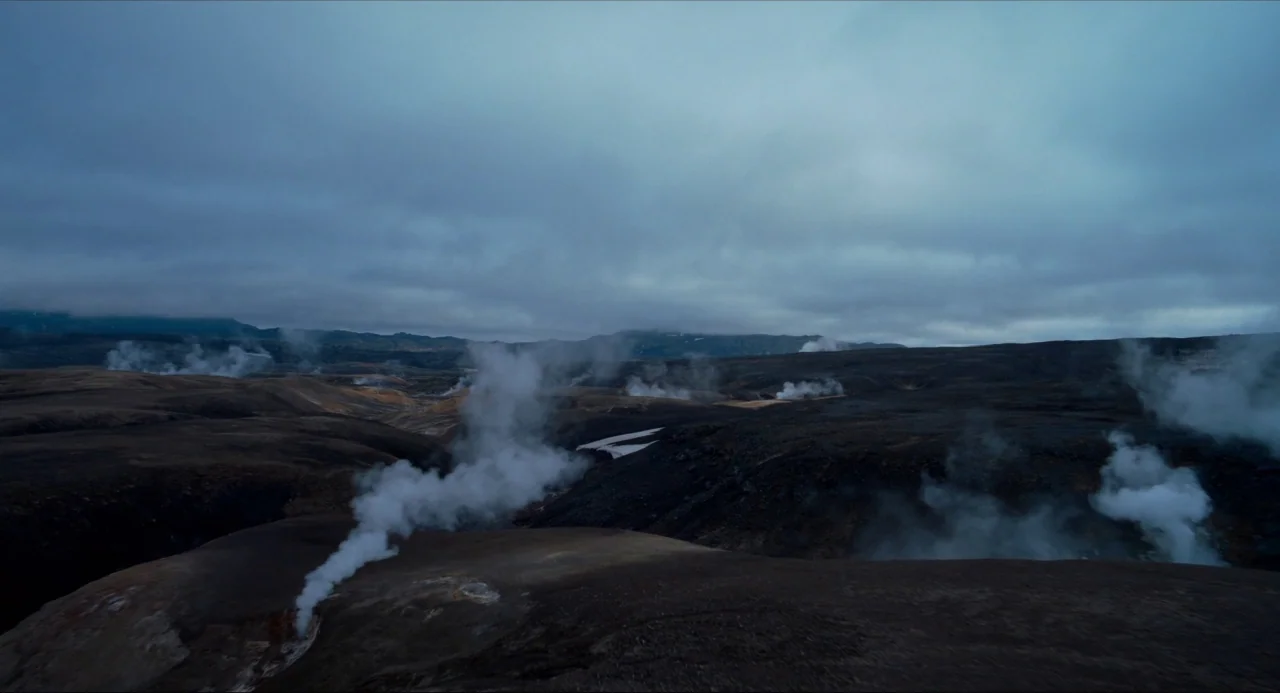 Voyage of Time (2016) movie still: establishing — A vast volcanic landscape features dark, rolling terrain punctuated by multiple geothermal steam…