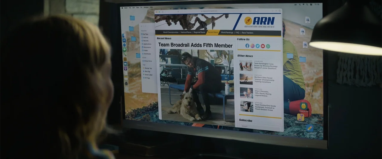 Arthur the King (2024) movie still: medium — A dimly lit room contains a person facing a large computer monitor displaying a website. The screen…