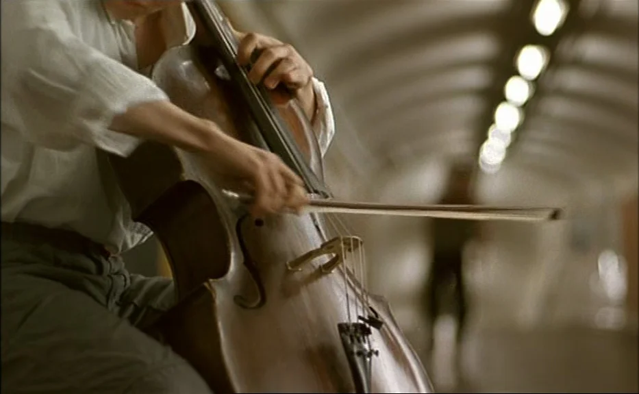 Les Amants Du Pont Neuf (The Lovers on the Bridge) (1991) movie still: medium — A person plays a cello in a long, curved tiled tunnel. Rows of…