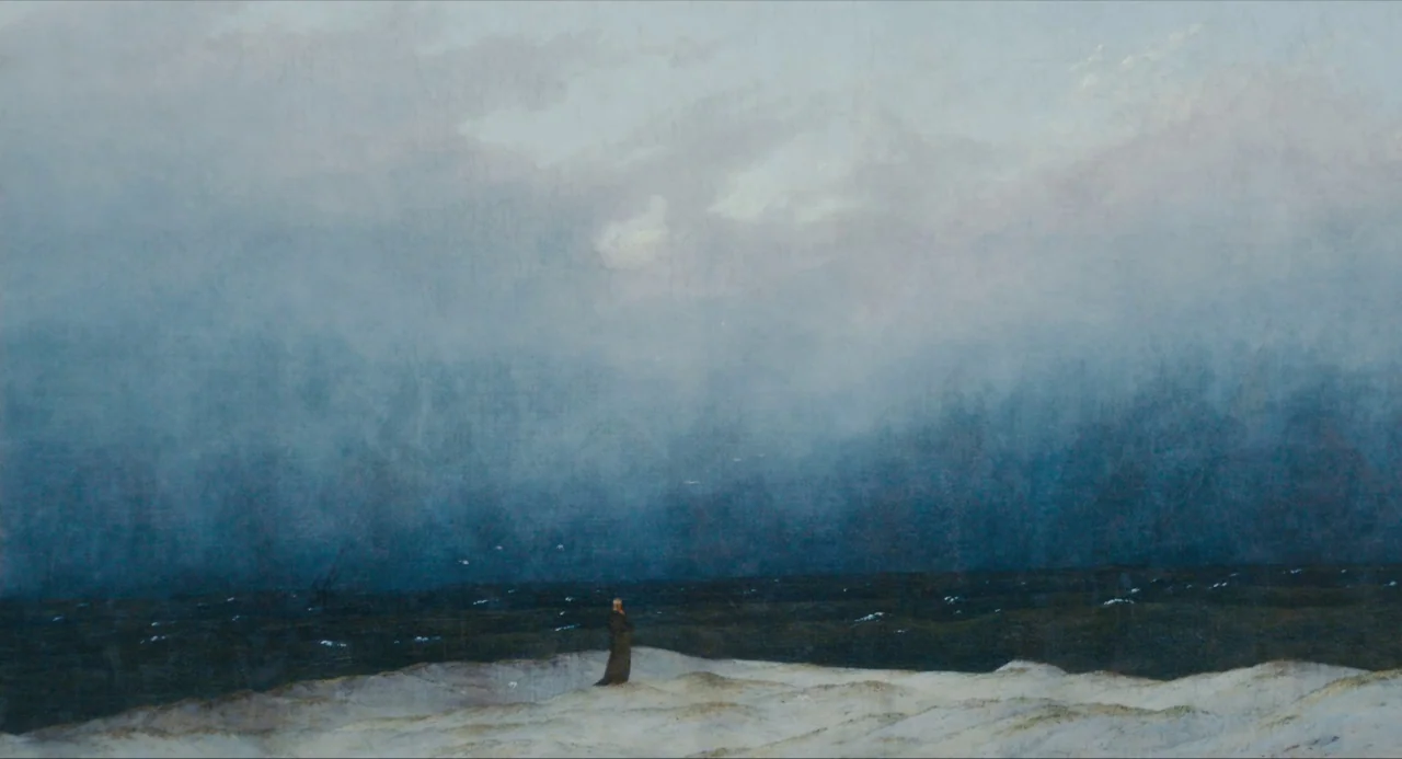 Submergence movie still: wide — A vast, desolate beach with sand dunes stretches under a heavy, overcast cloudy sky. A single small human figure…