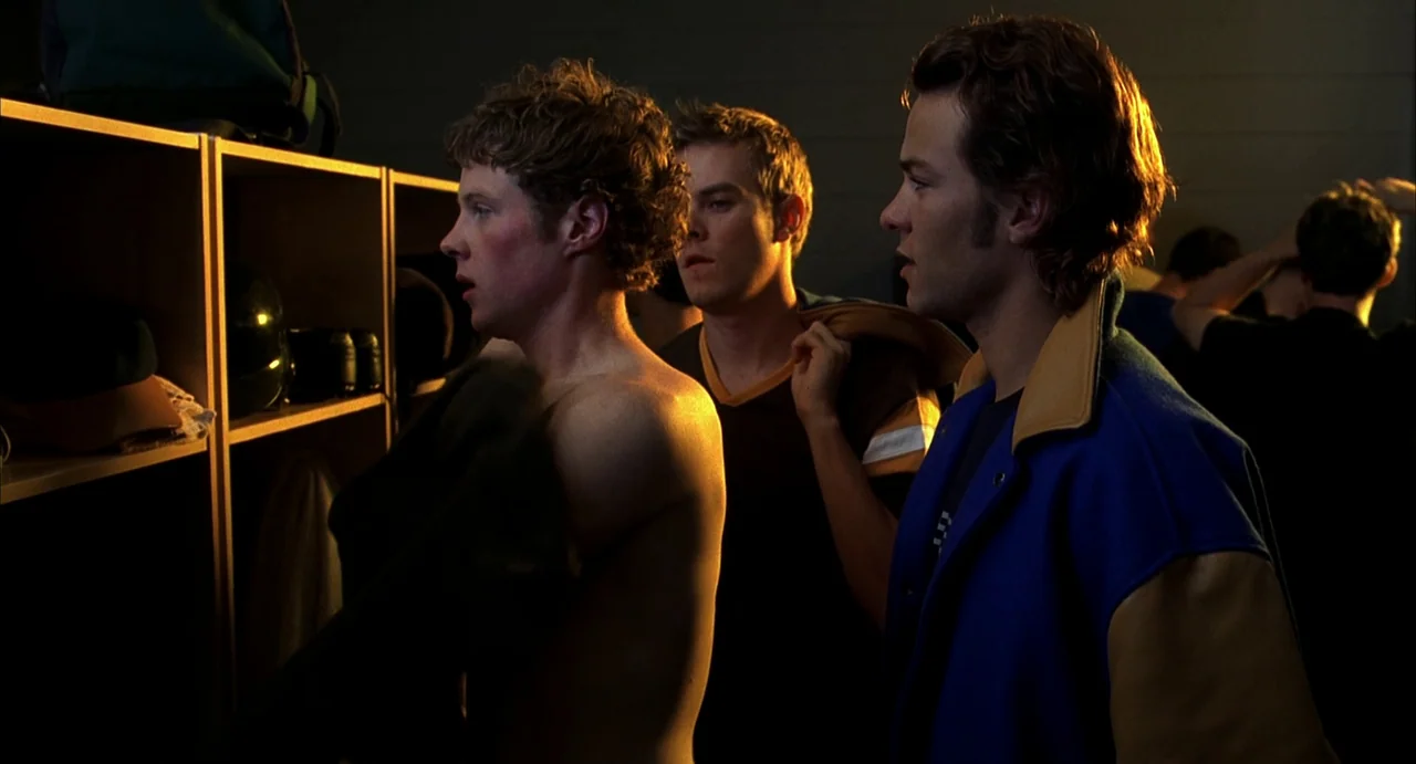 A History of Violence (2005) movie still: medium — A dimly lit locker room features rows of wooden storage compartments. Three young men stand in…