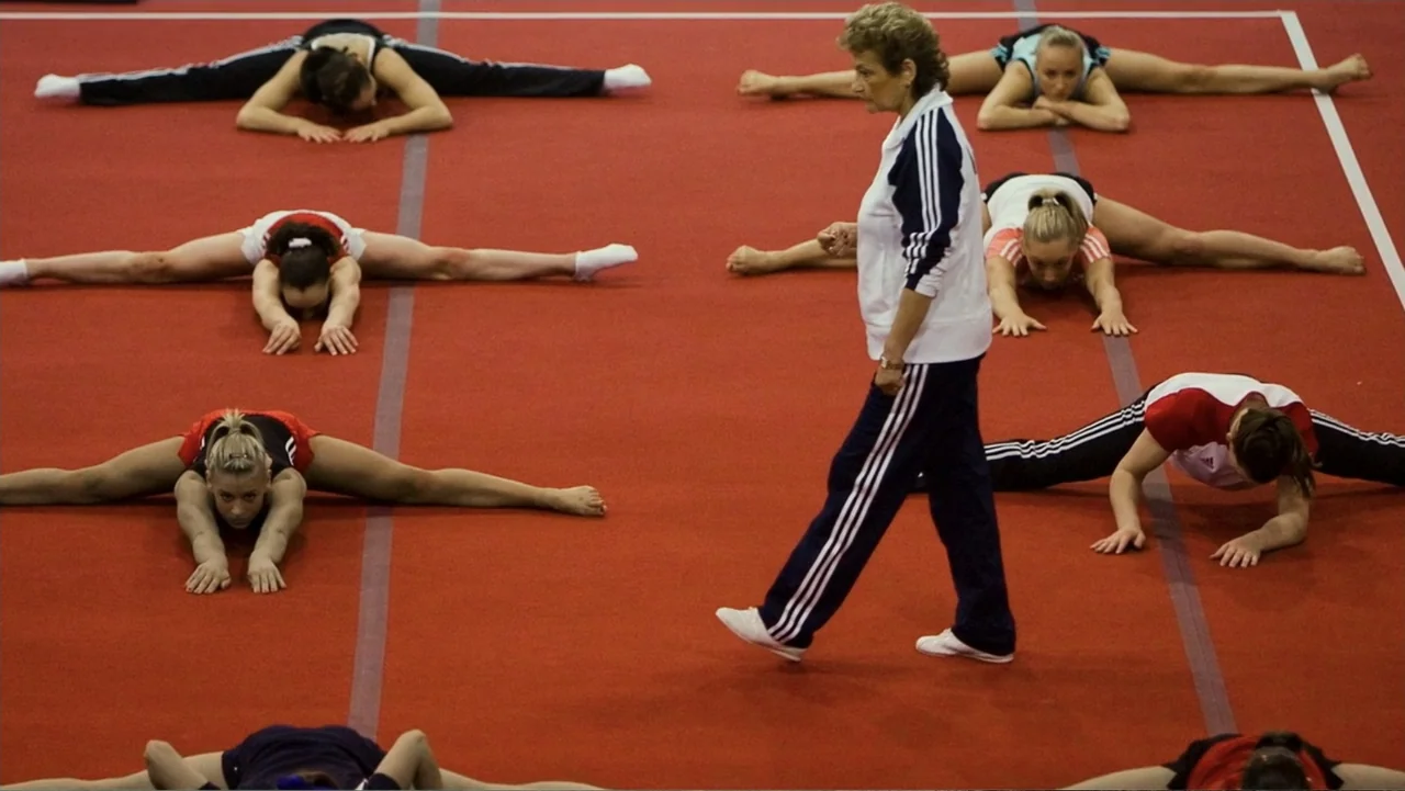 At the Heart of Gold: Inside the USA Gymnastics Scandal (2019) movie still: wide — An indoor gymnastics training center features a large red floor…