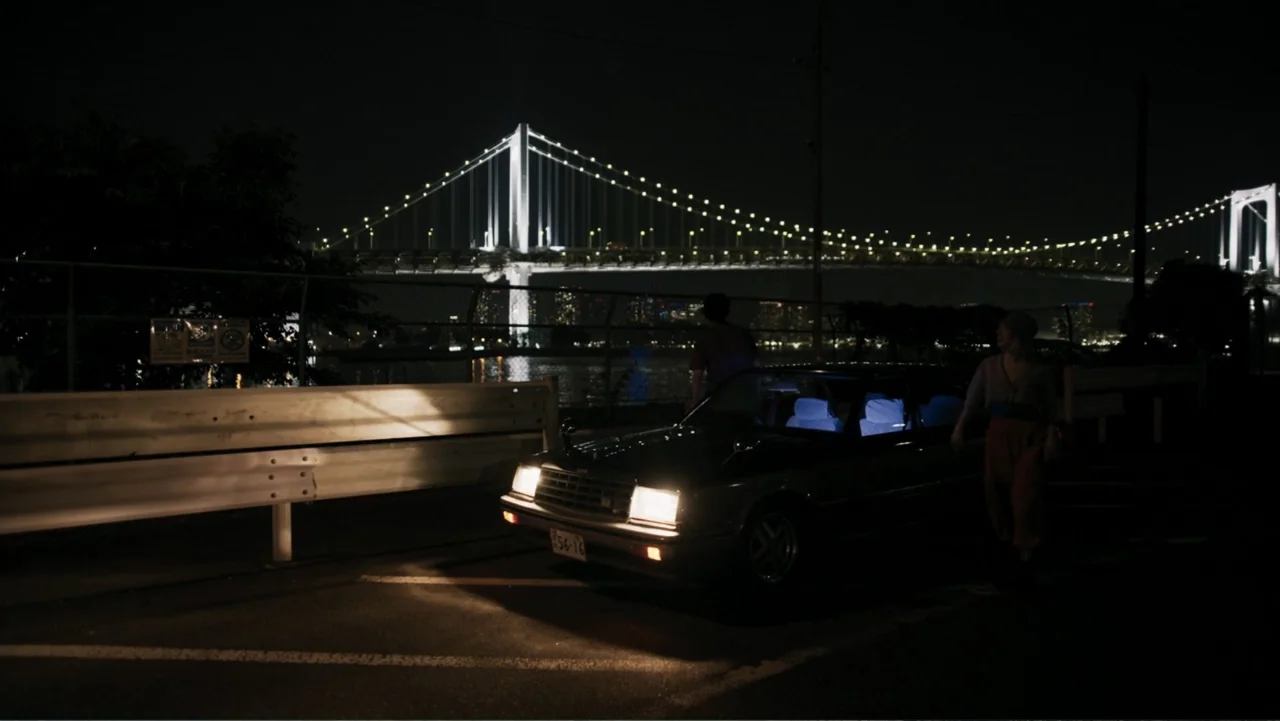 Victoria's Secret: The Tour '23 (2023) movie still: wide — A nighttime parking lot beside a fenced area overlooks a large illuminated suspension…