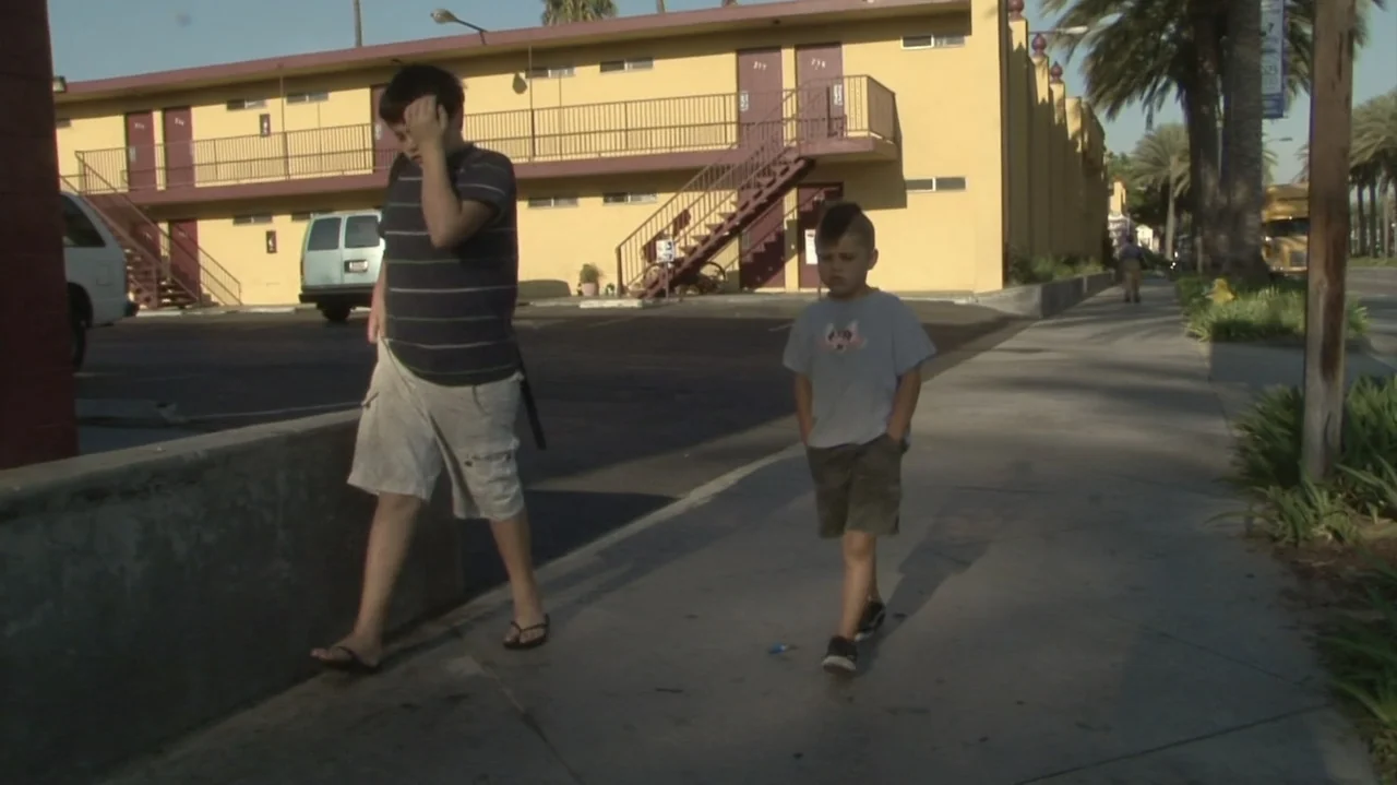 Homeless: The Motel Kids of Orange County (2010) movie still: fullbody — A low-rise yellow stucco motel features an external staircase and balcony…