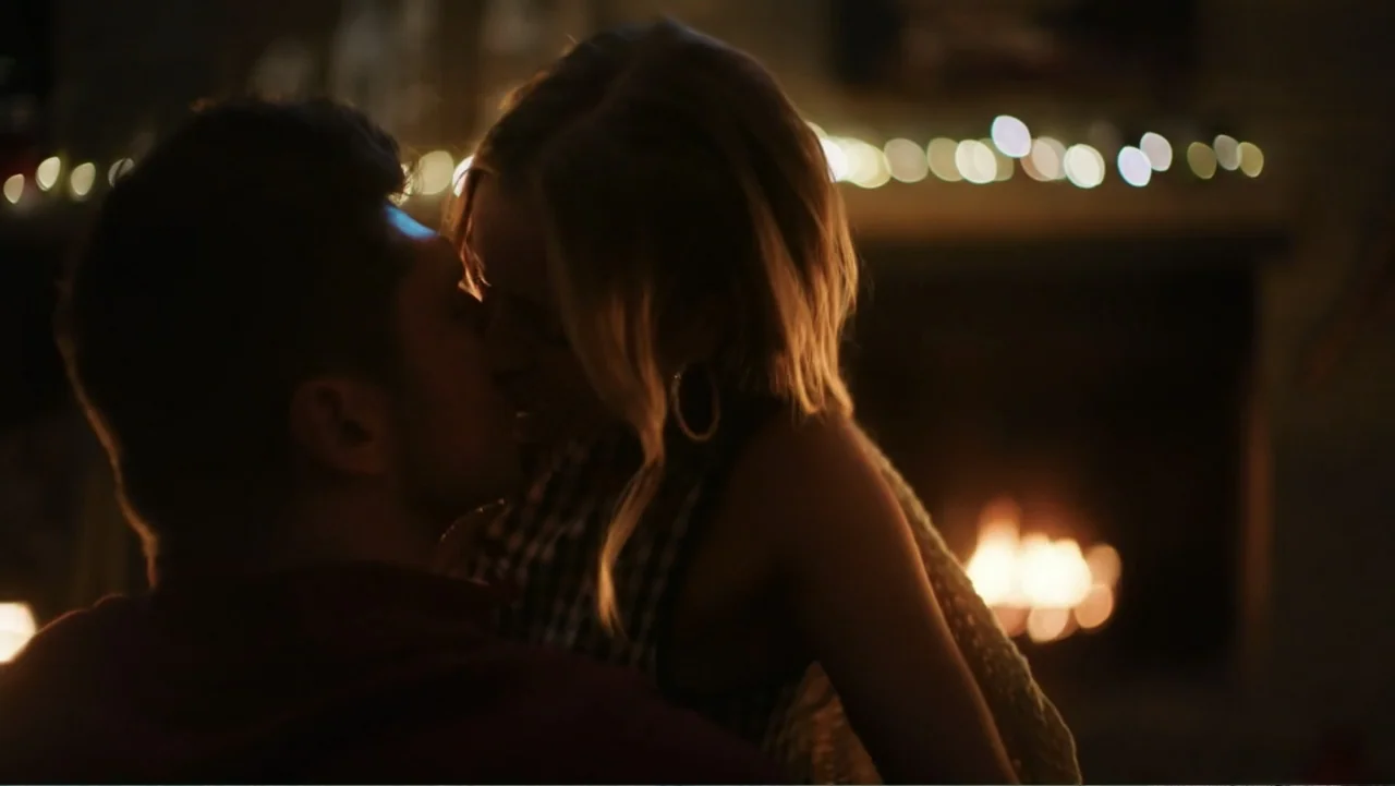 Christmas in the Spotlight (2024) movie still: medium — A dimly lit room features a glowing hearth with blurred festive fairy lights above. A couple…