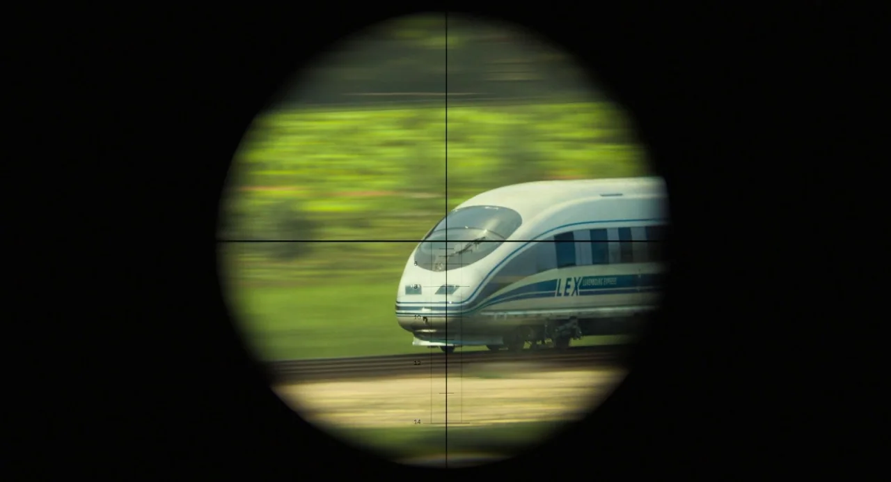 Gemini Man (2019) movie still: wide — A streamlined white passenger train travels along railway tracks through a green rural landscape. The frame is…