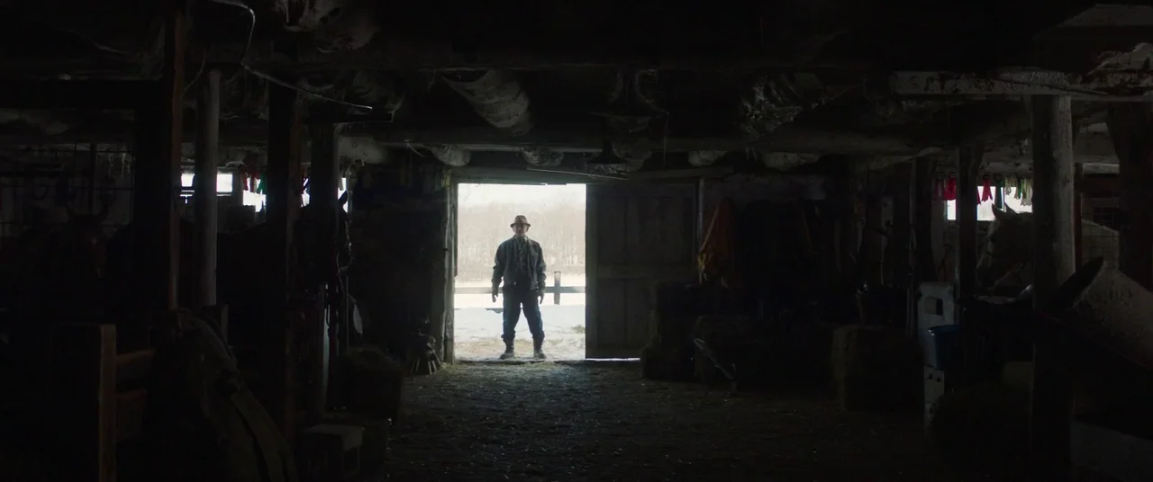 Falling (2020) movie still: fullbody — A dark wooden interior filled with shadows and hidden objects is visible. A lone man stands framed in the…