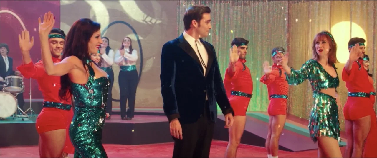 My Heart Goes Boom! (2020) movie still: medium — A 1970s variety show set features a brightly lit stage with sequined costumes. A male host stands…