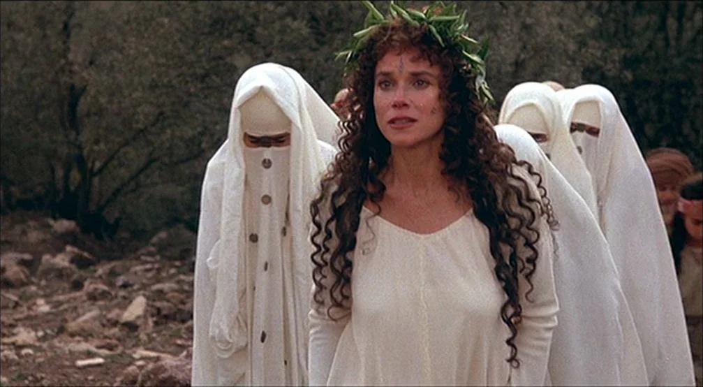 The Last Temptation Of Christ (1988) movie still: medium — An arid outdoor landscape features a group walking across a dusty brown path. A woman…