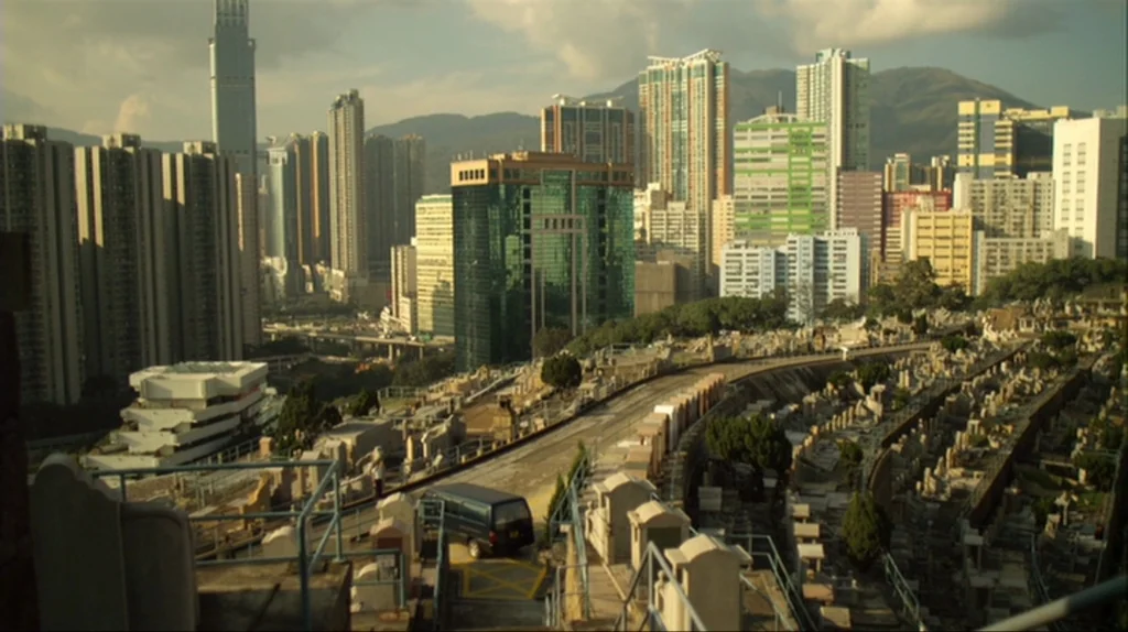 Contagion (2011) movie still: establishing — A dense hillside cemetery overlooks a massive, sprawling urban cityscape with high-rise apartment…