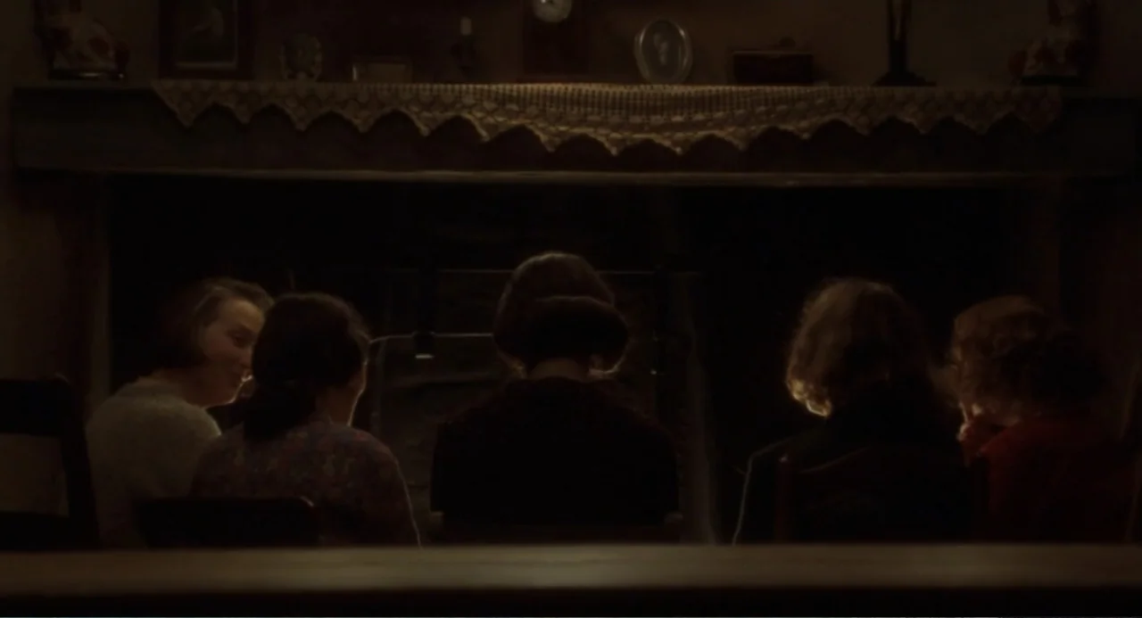 Dancing at Lughnasa (1998) movie still: medium — A dimly lit room features a large stone fireplace with a mantle shelf above. Five women sit in a…