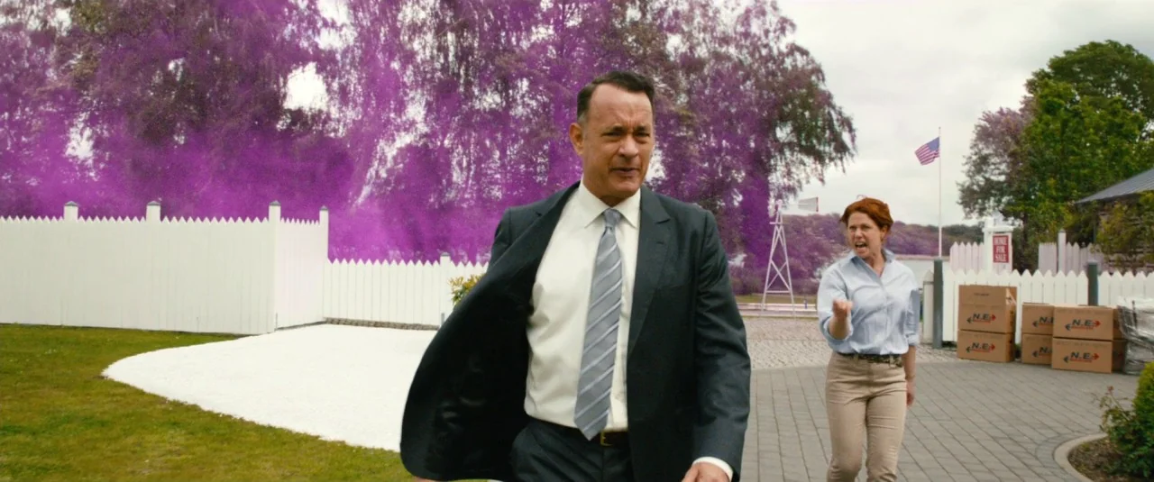 A Hologram for the King movie still: medium — A suburban residential driveway features a white fence and a stack of moving boxes. A man in a suit…