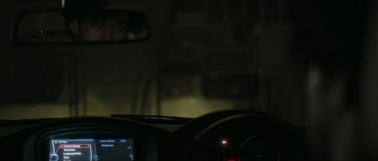Innocent Vengeance (2023) movie still: medium — A dark vehicle interior with a glowing digital dashboard display visible in the foreground. A man's…
