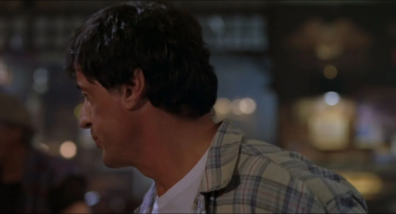 Cop Land (1997) movie still: medium — A dimly lit indoor space features a man in a plaid shirt. The man stands in profile while looking toward the…