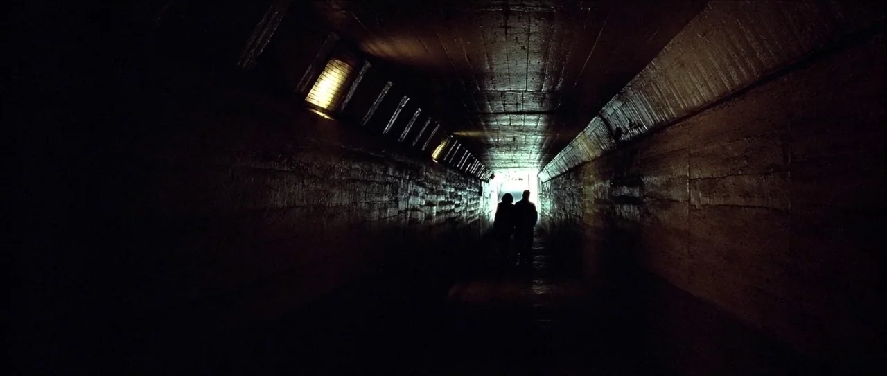 Lady Vengeance (2005) movie still: wide — A long concrete underpass features rough-textured walls and rectangular lights inset into the ceiling. Two…