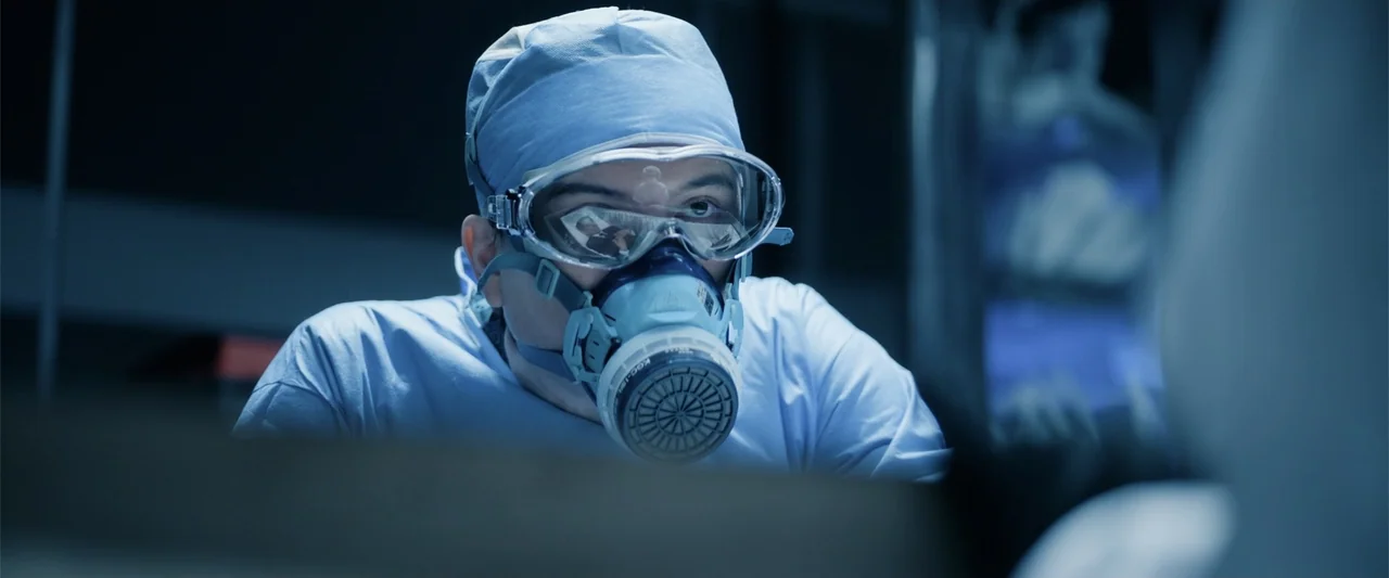 Angel Flight THE MOVIE (2026) movie still: closeup — A clinical environment with sterile medical equipment visible in the blurred foreground. A male…