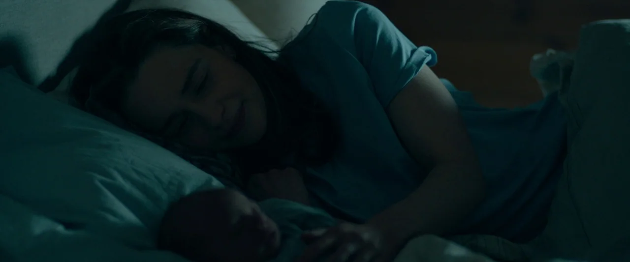 The Pod Generation (2023) movie still: medium — A woman lies on a mattress with white sheets in a darkened room. She rests her eyes while lying…