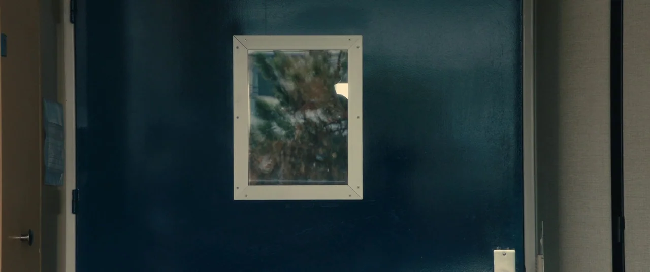 BPM (Beats Per Minute) (2017) movie still: medium — A dark blue industrial-style door features a centered square window frame. Reflections of green…